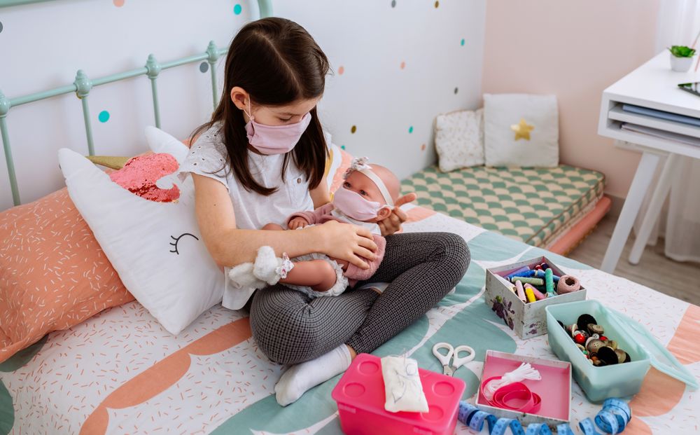 Girl with mask playing to take care of her baby doll with mask
