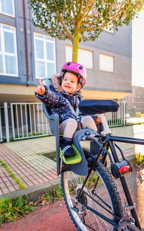 Portrait of little girl with pink helmet on pointing in bike seat ready for ride