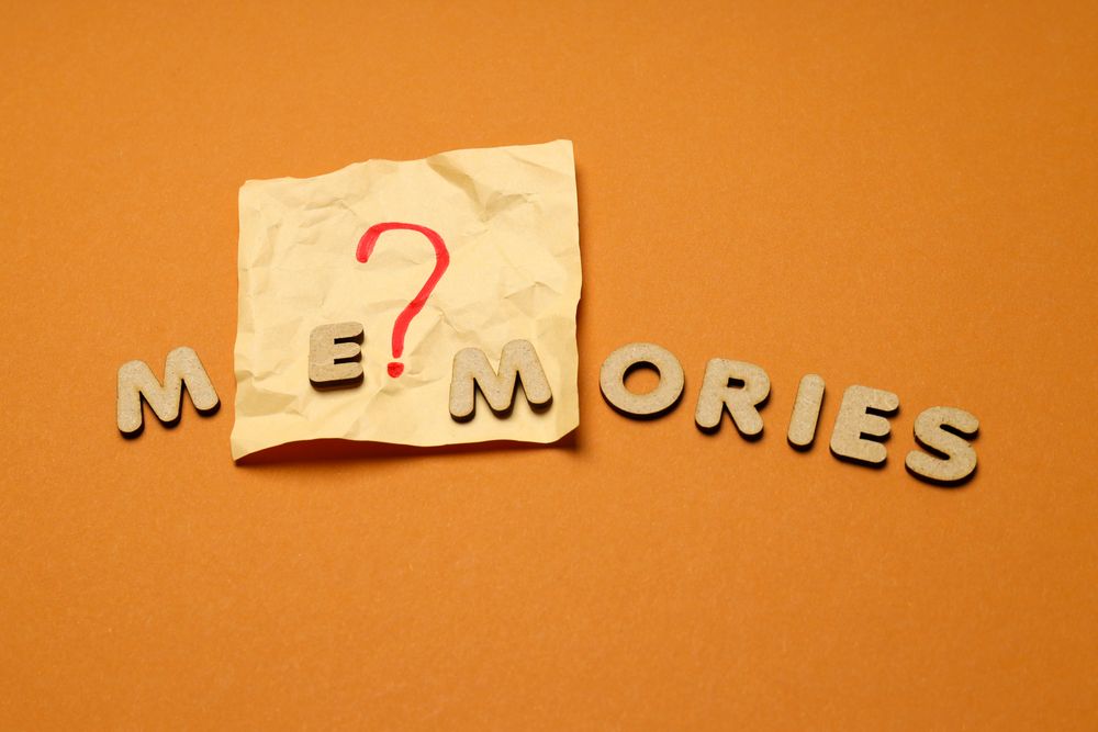 The word “Memories” written in cork on top of post it note in center of dusty orange background