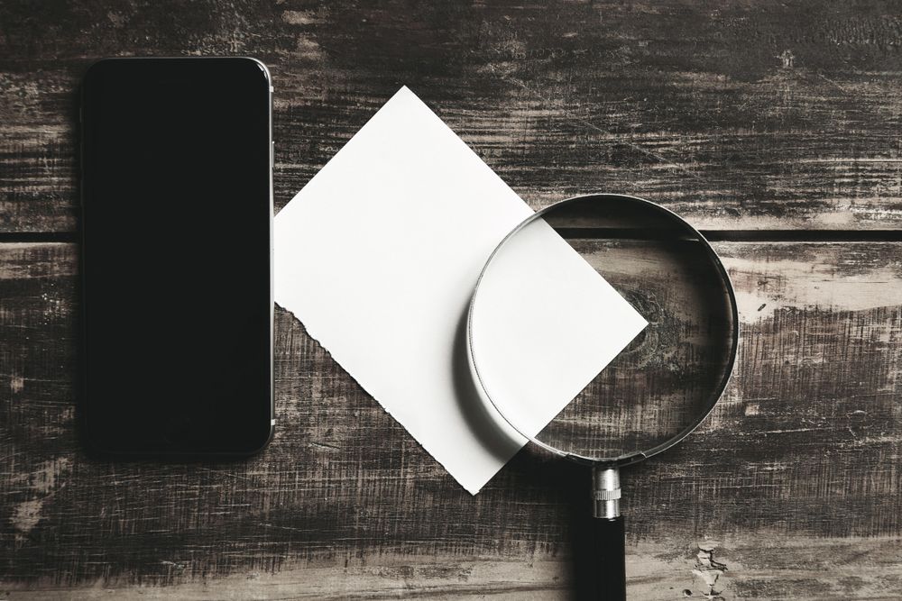 Top view of paper, cell phone magnifying glass on wooden table