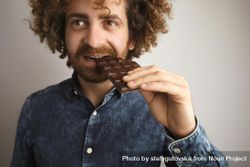 Man with curly hair biting into chocolate bar 49WrW0