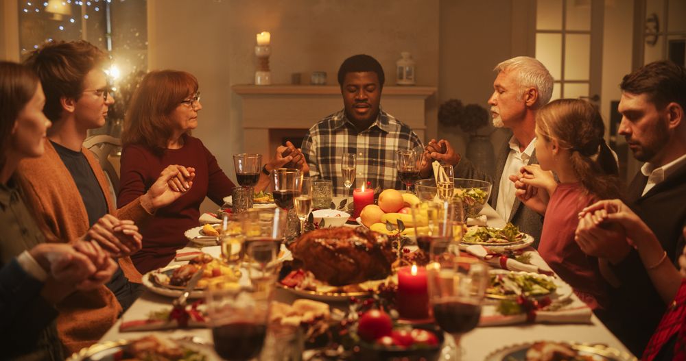 Portrait of a Young Black Man Sitting at a Festive Table with Family and Friends, Praying Before Eating a Turkey Dinner.