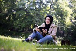 Relaxed Middle Eastern woman with book sitting on the grass 4jZM94