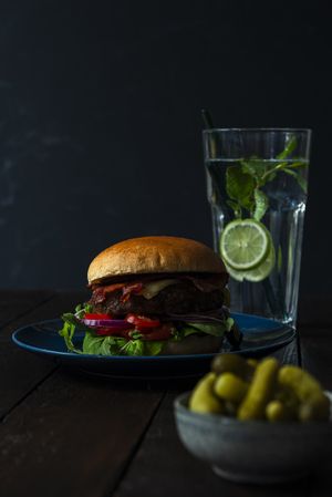 Burger on a blue plate water and pickels on dark
