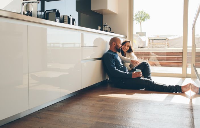 Young man and woman sitting on floor in kitchen and talking