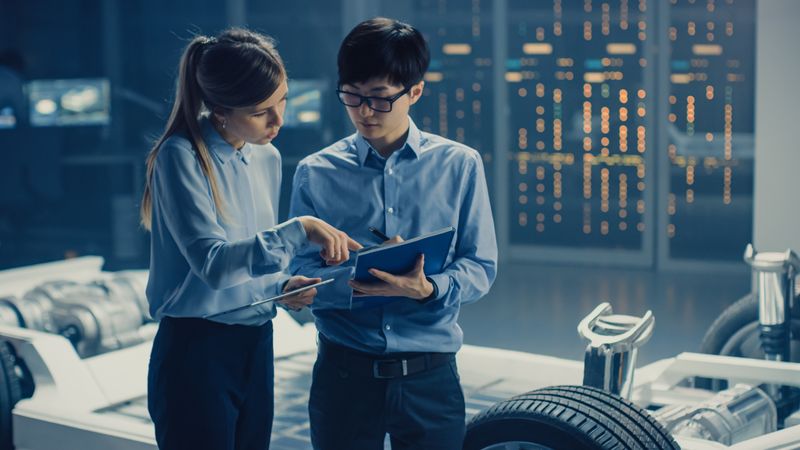 Male and Female Automobile Design Electric Car Engineers Having Conversation, Use Clipboard to Check Maintenance Issues.