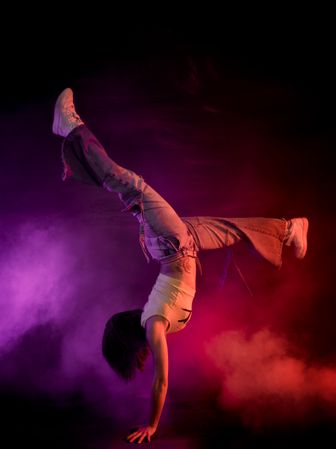 Young woman break dancing in colorful smoke