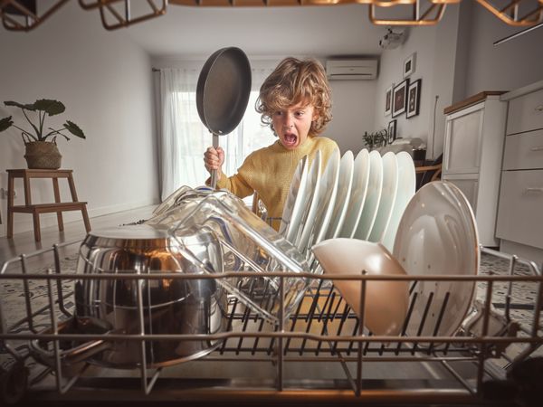 Positive boy with frying pan near dishwasher