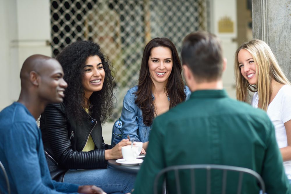 Group of friends sitting in outdoor cafe together with coffee