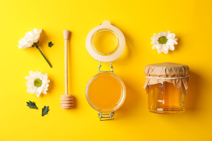 Flat lay. Jars with honey, dipper and chamomile on yellow background, copy space