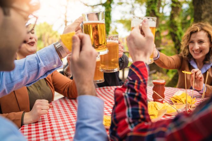 A group of five friends come together outdoors, raising their beer mugs in a toast