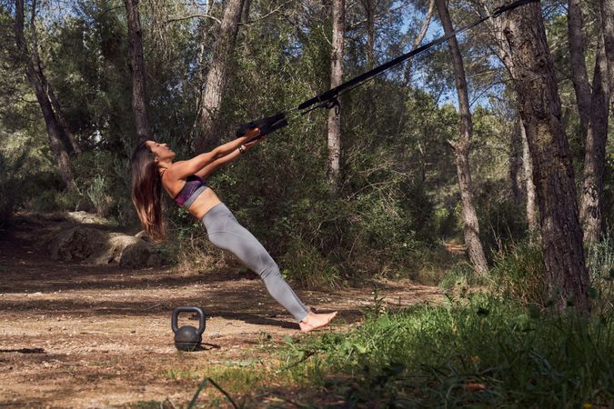 Fit woman exercising in woods using TRX bands