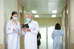 Doctors wearing protective mask discussing and consulting patient case over a smart phone
