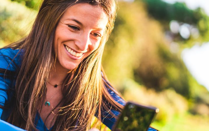 portrait of young woman using smartphone sitting on grass in park