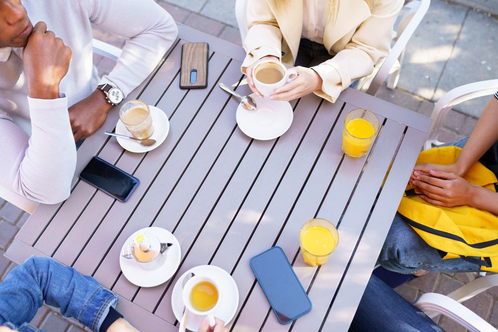 Looking down at hands of friends with coffee and juice at outdoor table
