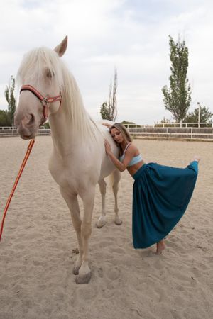 woman in skirt leaning on horse side while dancing at paddock