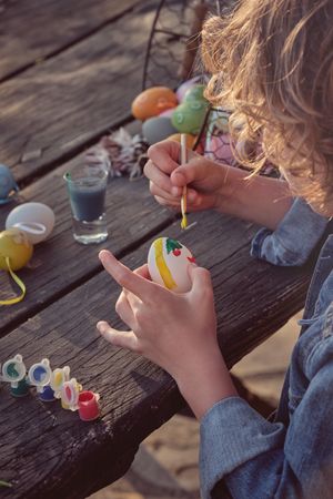 Boy painting eggs for Easter on wooden table