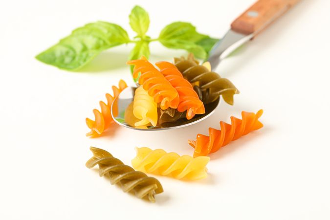 Spoon with color pasta on plain background, space for text and closeup