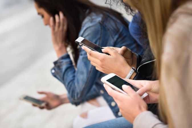 Close up of women using smart phones sitting outside