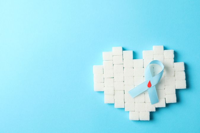 Diabetes awareness ribbon and heart made of sugar cubes on blue background