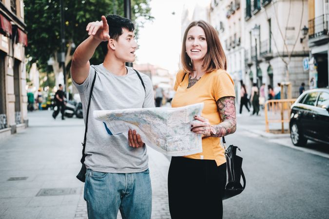 Joyful multiracial tourists checking map and standing on urban street