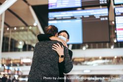 Female in face mask hugging her husband at airport 5kaz6b