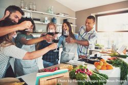 Multiethnic friends toasting red wine while cooking in a bright kitchen 5lBKeb