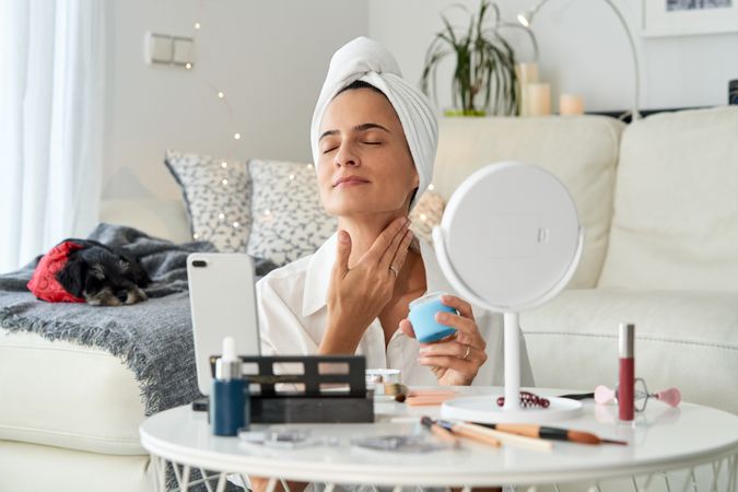 Glad woman vlogger applying cream on neck while recording video