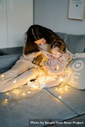 Mother and baby sitting on bed and playing with string light 5lWxa0