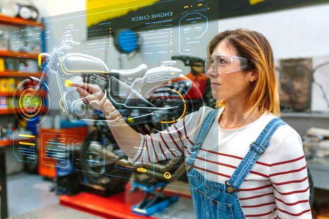 Female mechanic using hud panel screen with augmented reality hologram to review motorcycle
