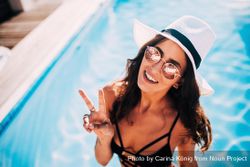 Young woman making peace sign on a sunny day by the pool A492Lb
