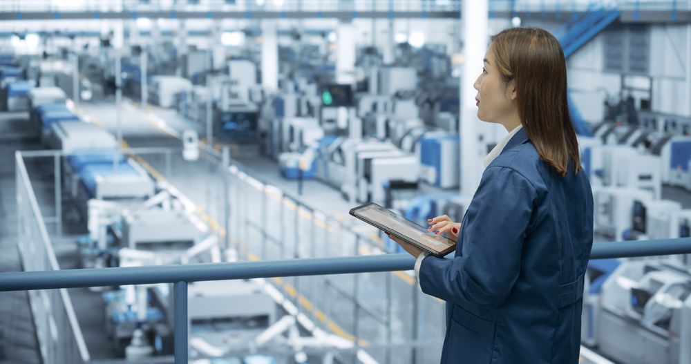 Portrait of a Japanese Engineer Using Tablet Computer and Looking Around a Factory Facility with Equipment Producing Modern Electronic Components for Different Industries