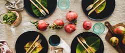 Fresh table setting on brown table cloth, leaves on dark plates, pomegranate, wide composition