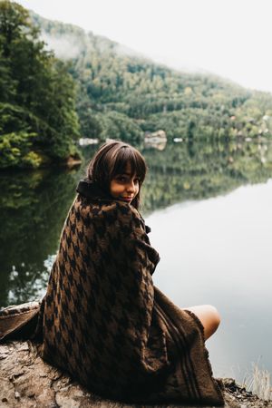 Woman sitting with blanket near lake and mountains