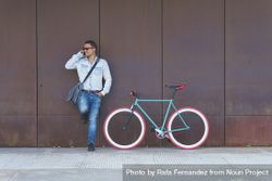 Male in sunglasses standing with red and green bicycle leaning on wall and talking on phone 5ny720