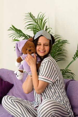 Woman in striped pajamas hugs plush bear, smiling warmly.