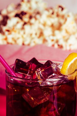 Popcorn in bowl near drink in glass with ice and lemon