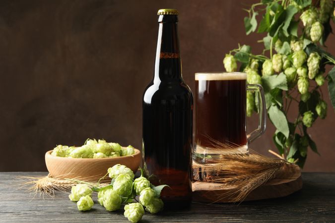 Beer, hop and wheat on wooden table against brown background