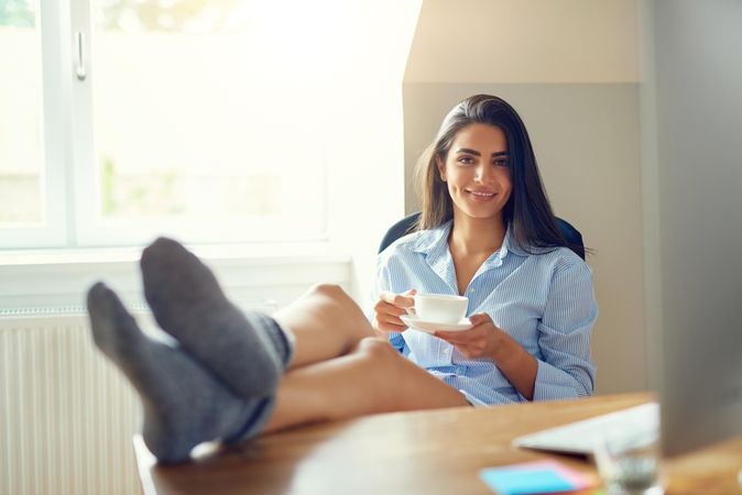 Smiling Arab woman sitting at her desk with feet up sipping tea