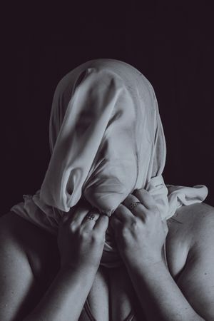 Grayscale portrait of woman covering her face with textile