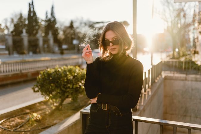 Stylish woman lighting cigarette near metro station