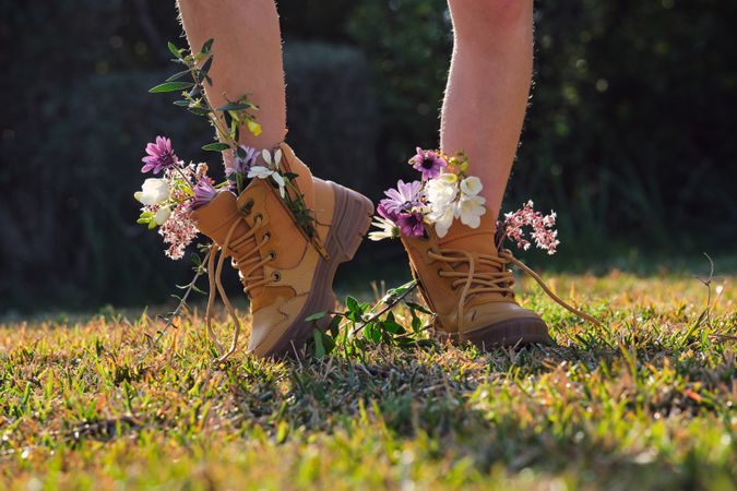Crop person wearing boots with flowers on grassy lawn