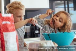 Little kids mixing batter in a bowl for baking, with girl licking a spoon 5oEK1b