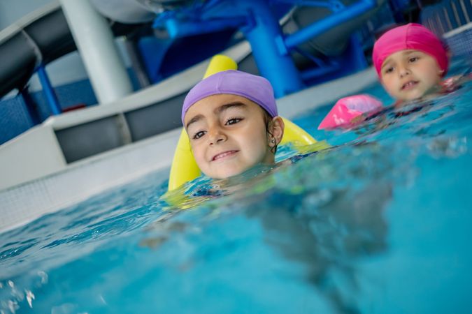 Cheerful girl in hat smiling and swimming in pool in water park