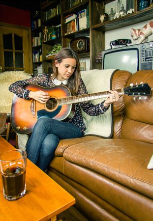 Young hipster woman playing acoustic guitar at home