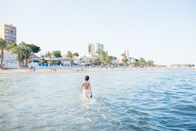 Boy walking in blue water of resort sea