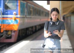Young female traveler holding a tablet standing on a train platform 4mqR74