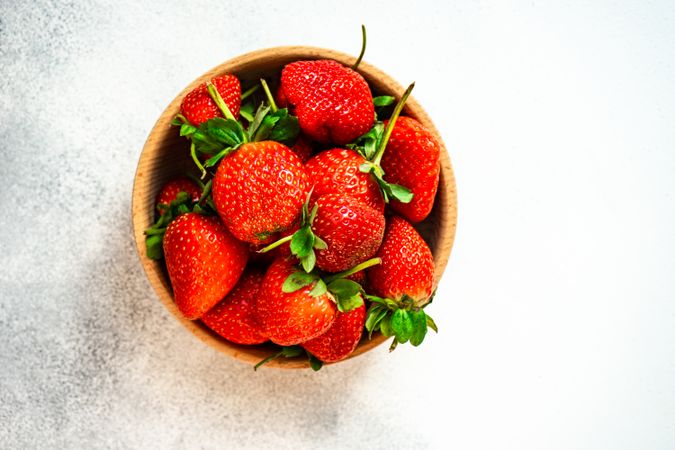 Top view of strawberries in wooden bowl full on grey counter with copy space