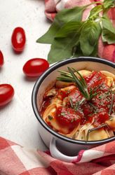 Bowl of delicious ravioli with tomato sauce and rosemary on table cloth