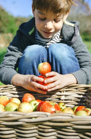 Smiling boy playing with apples over a wicker basket